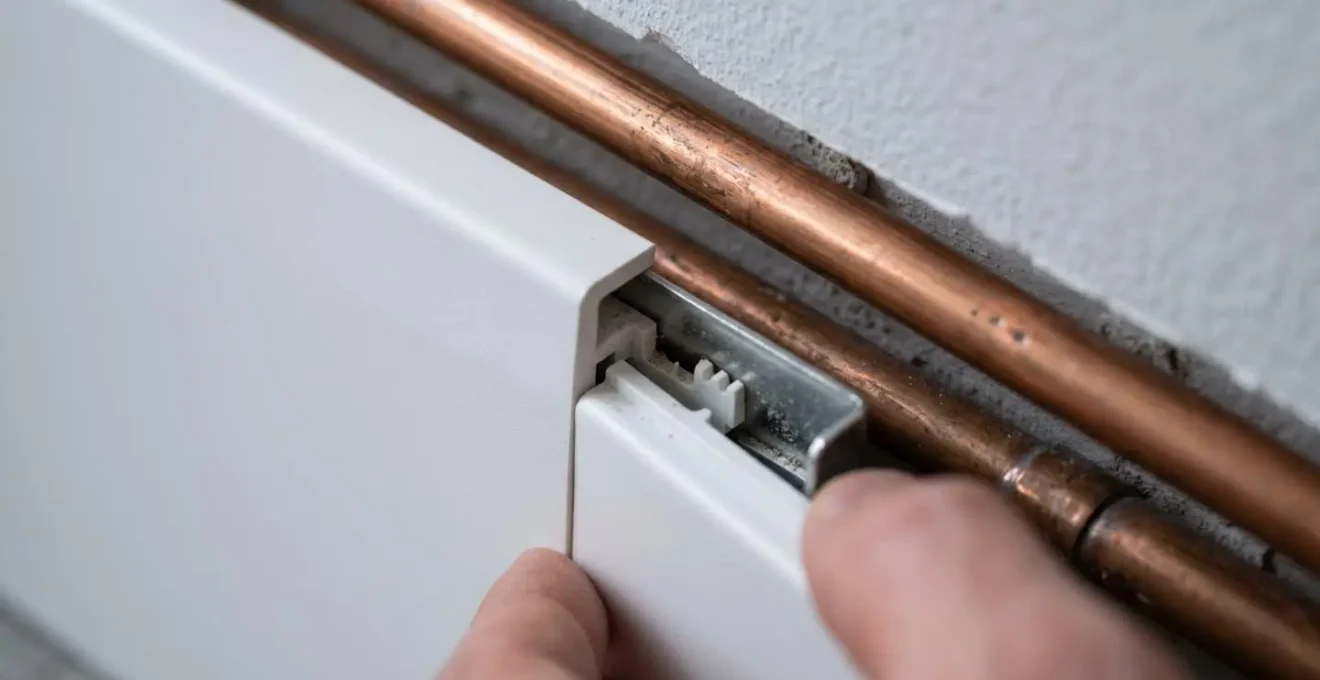 Installation de plinthes techniques blanches dissimulant des tuyaux le long d'un mur